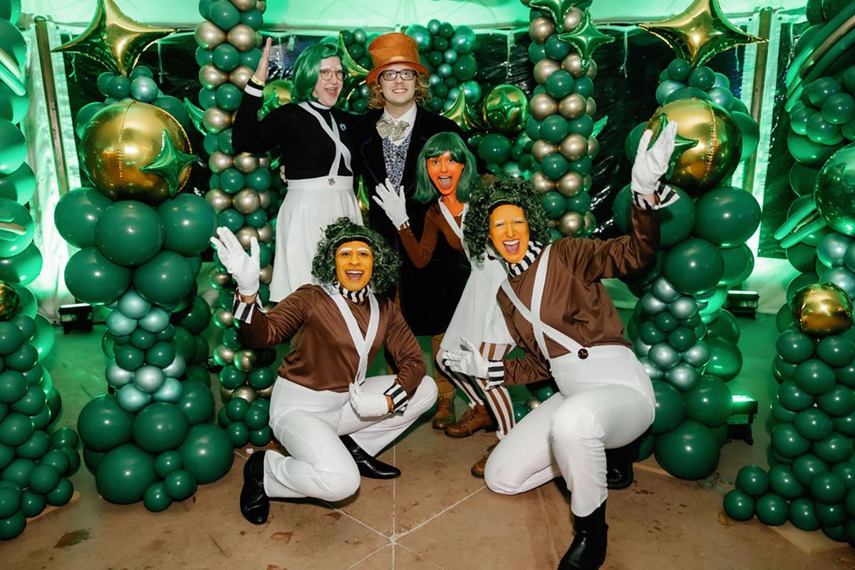 Group in costume surrounded by green balloons.