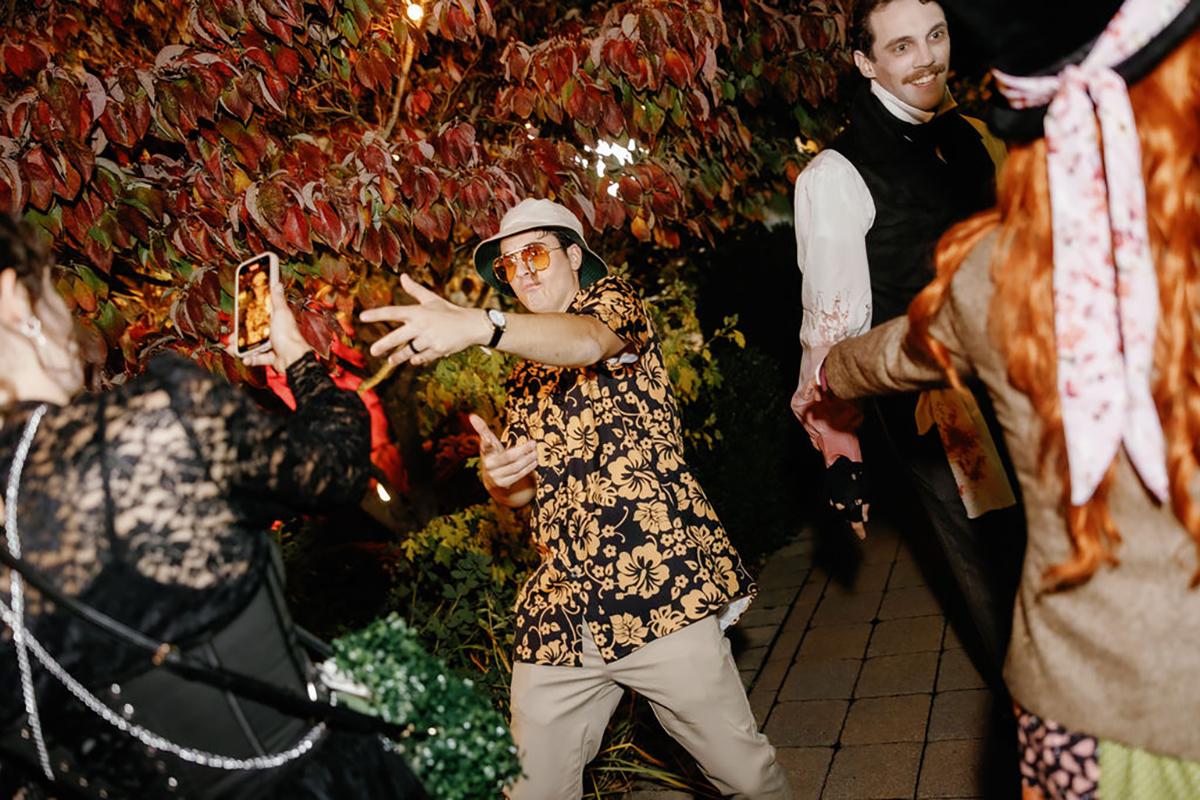 People in costumes dancing outdoors at night, surrounded by colorful leaves.