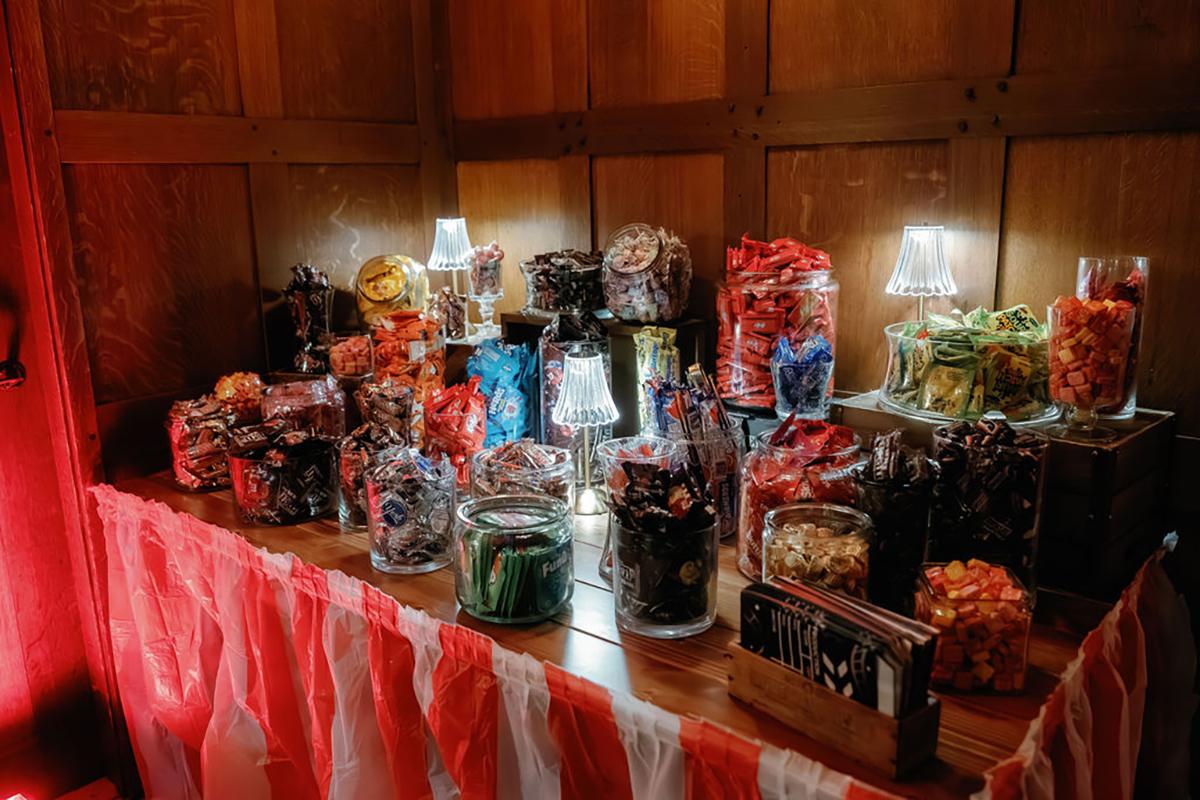 Candy jars on a striped tablecloth, warmly lit in a wooden room.