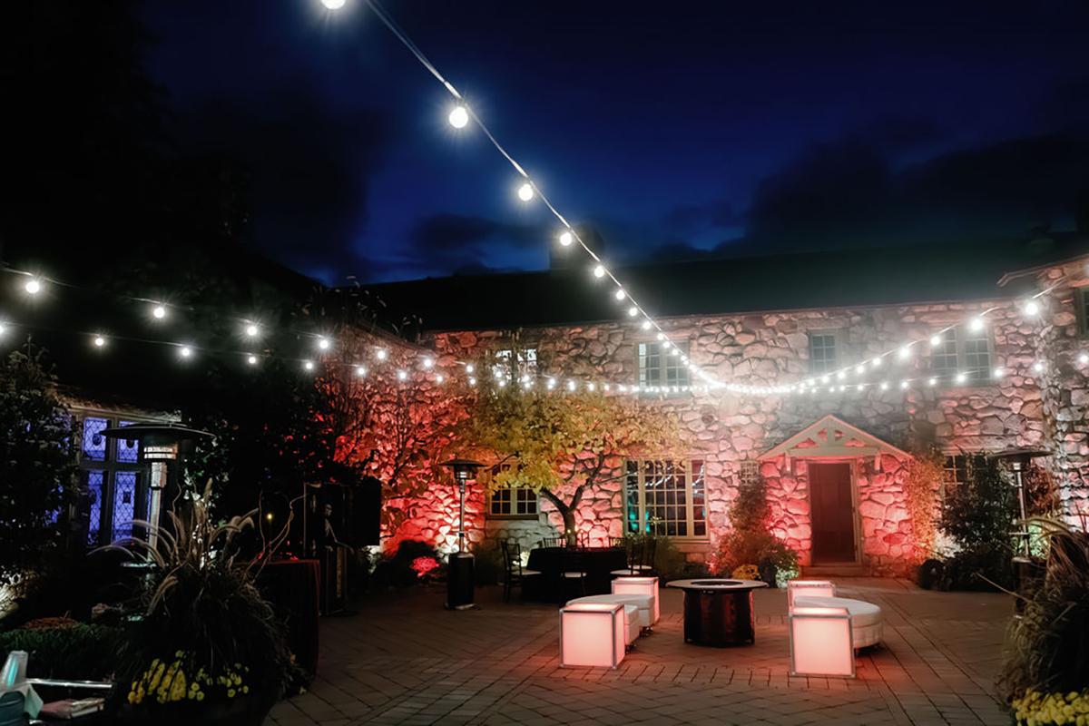 Courtyard at night, string lights overhead, and a brick building illuminated in red.