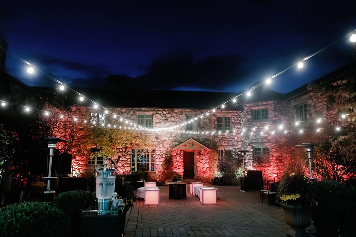 Courtyard with string lights at nighttime. Brick walls illuminated with red lights.
