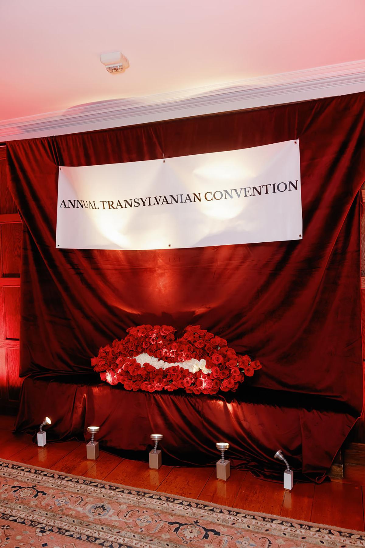 Red draped backdrop with banner and red floral wreath display.