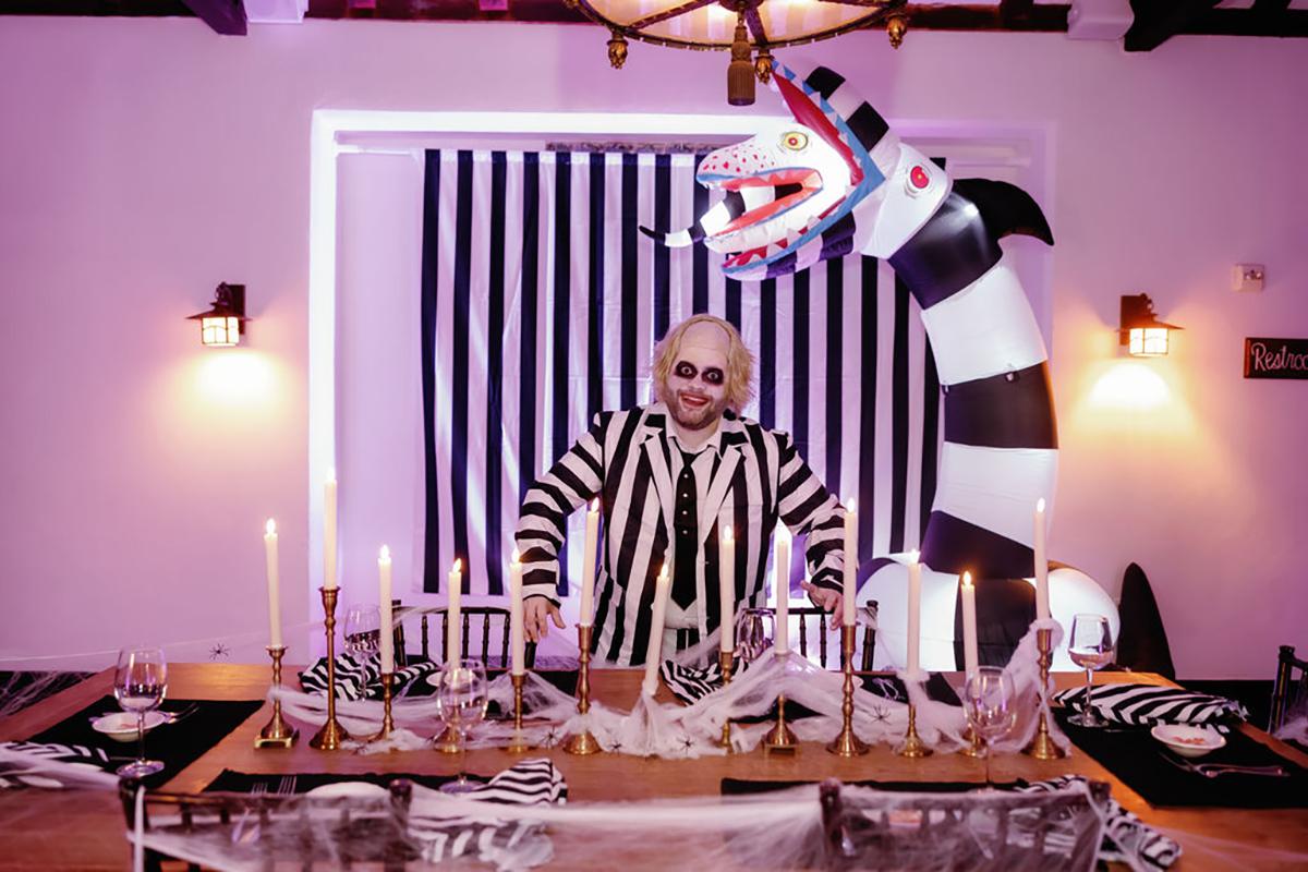 A man in a black and white striped outfit stands by a decorated table with candles.