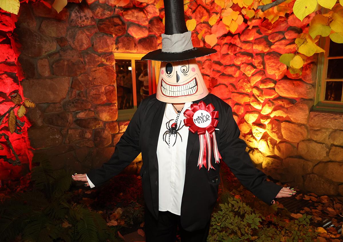 Mascot character in formal attire, standing against a stone wall with warm lighting.