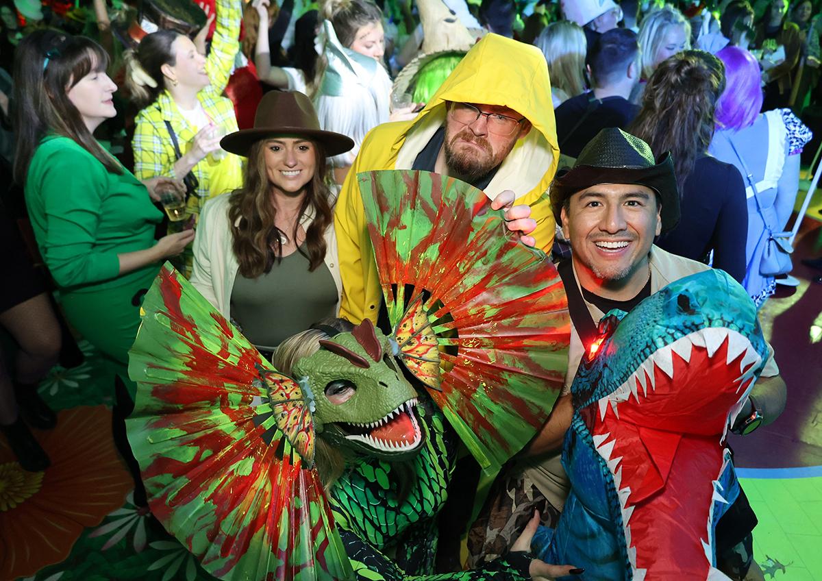 Costumed group at a lively party, wearing dinosaur and explorer outfits.