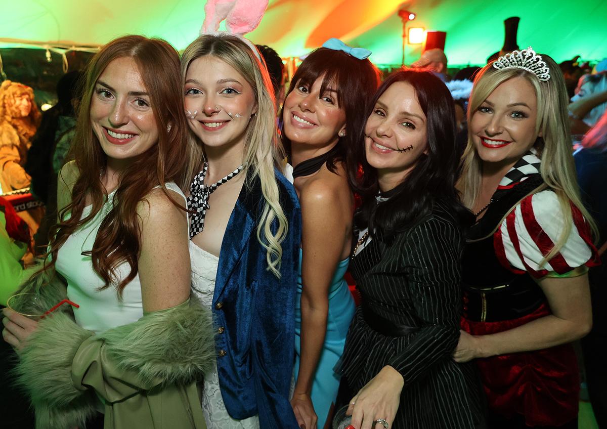 Five women in costumes posing and smiling at a party.