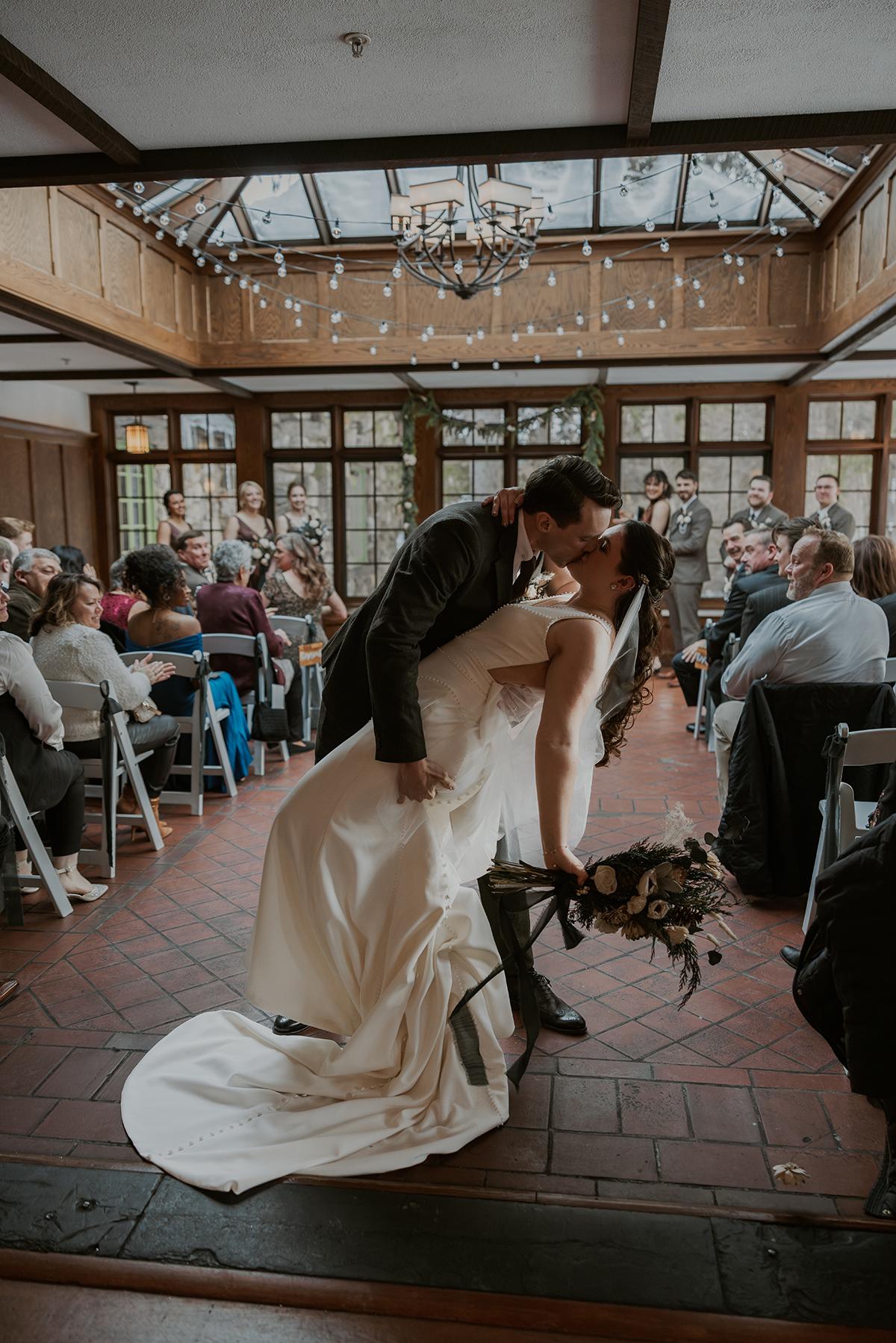 Bride and groom kissing passionately in a decorated indoor venue.