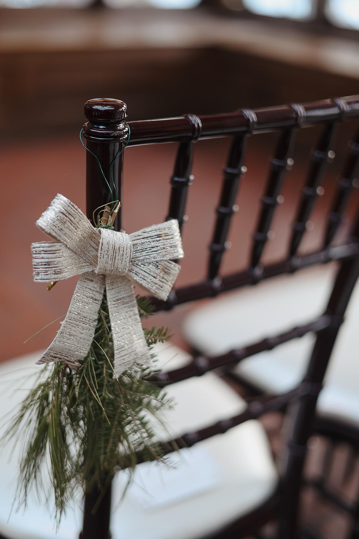 Wooden chair decorated with a burlap bow and greenery.
