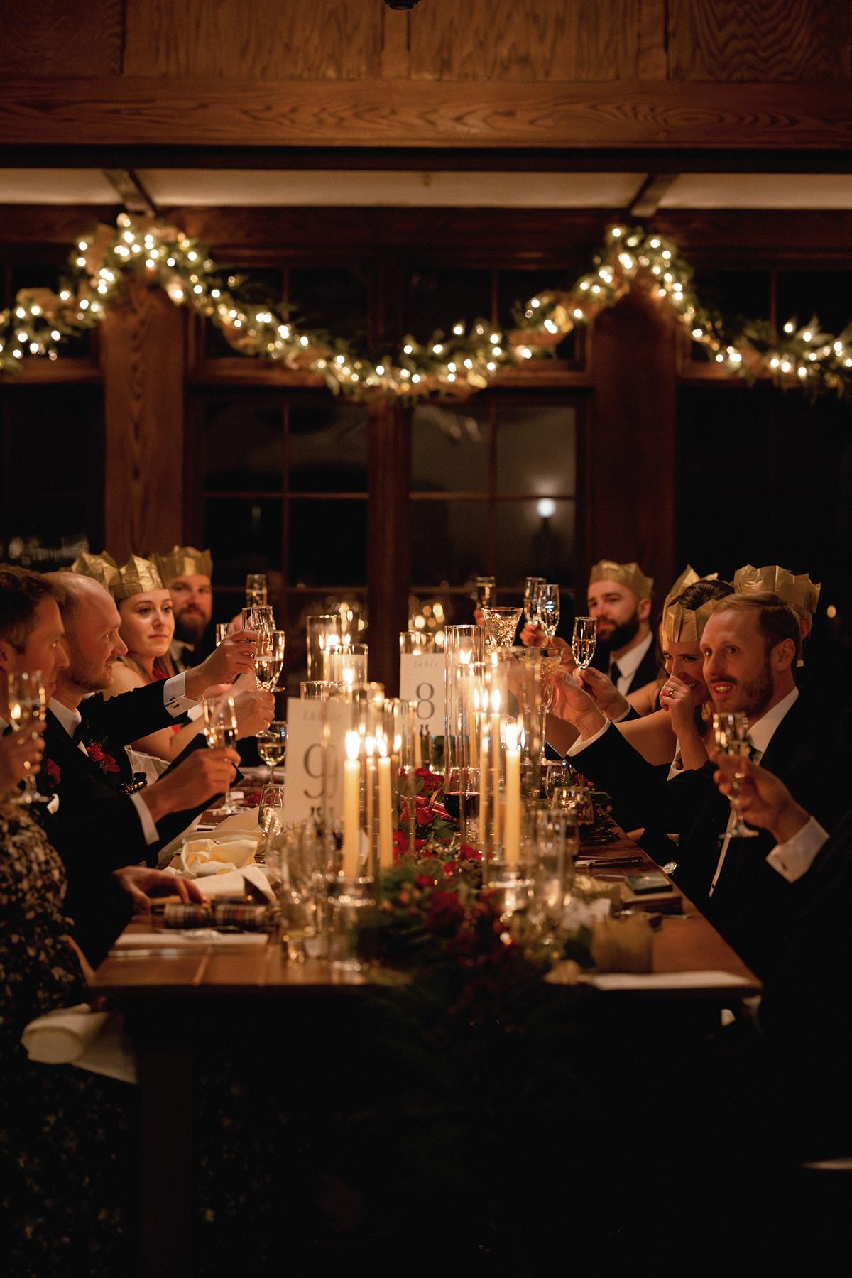 Candlelit dinner with people toasting, festive garlands above.