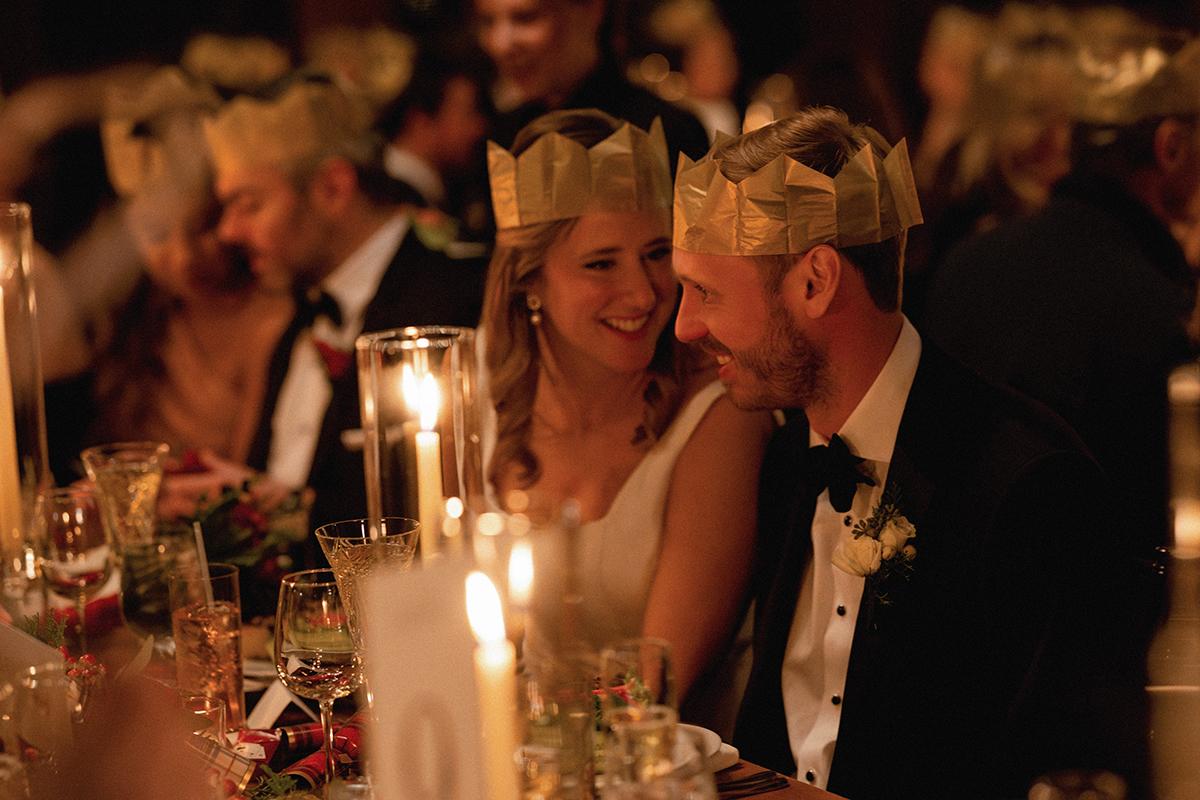 Guests wearing paper crowns, smiling at a candlelit dinner.