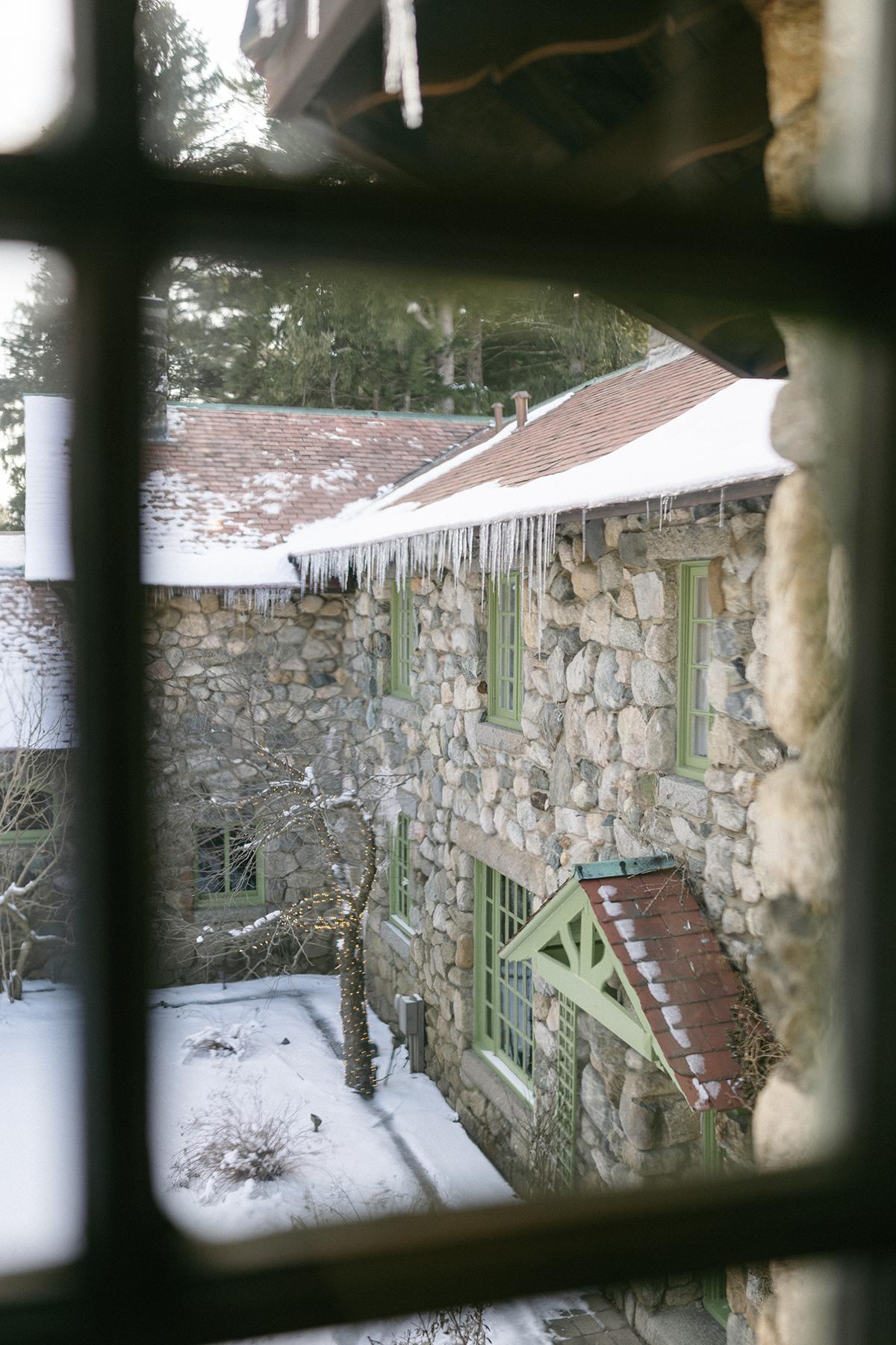 Stone house with snowy roof seen through a window.