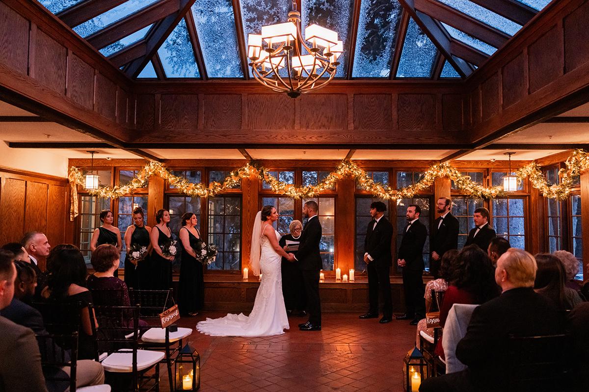 Bride and groom exchange vows in a warmly lit, decorated hall.