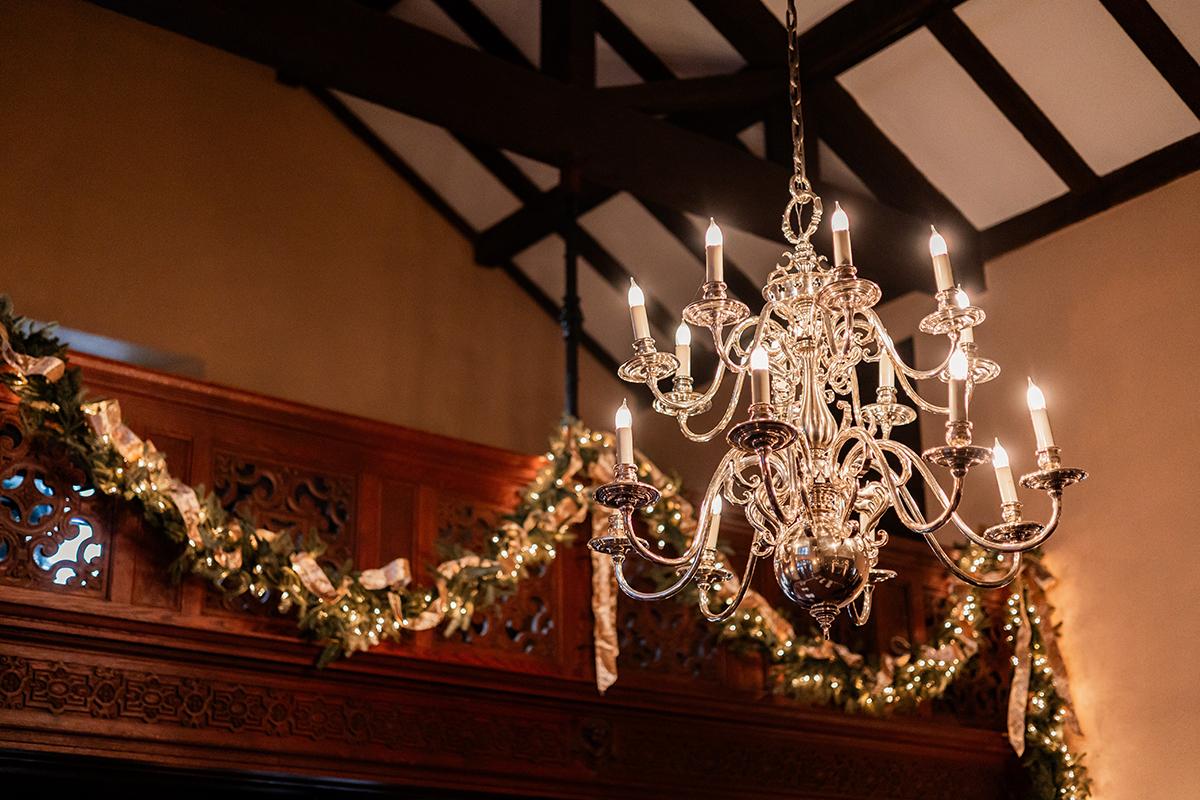 Elegant chandelier with warm lights, garland, and festive decor in a dimly lit room.