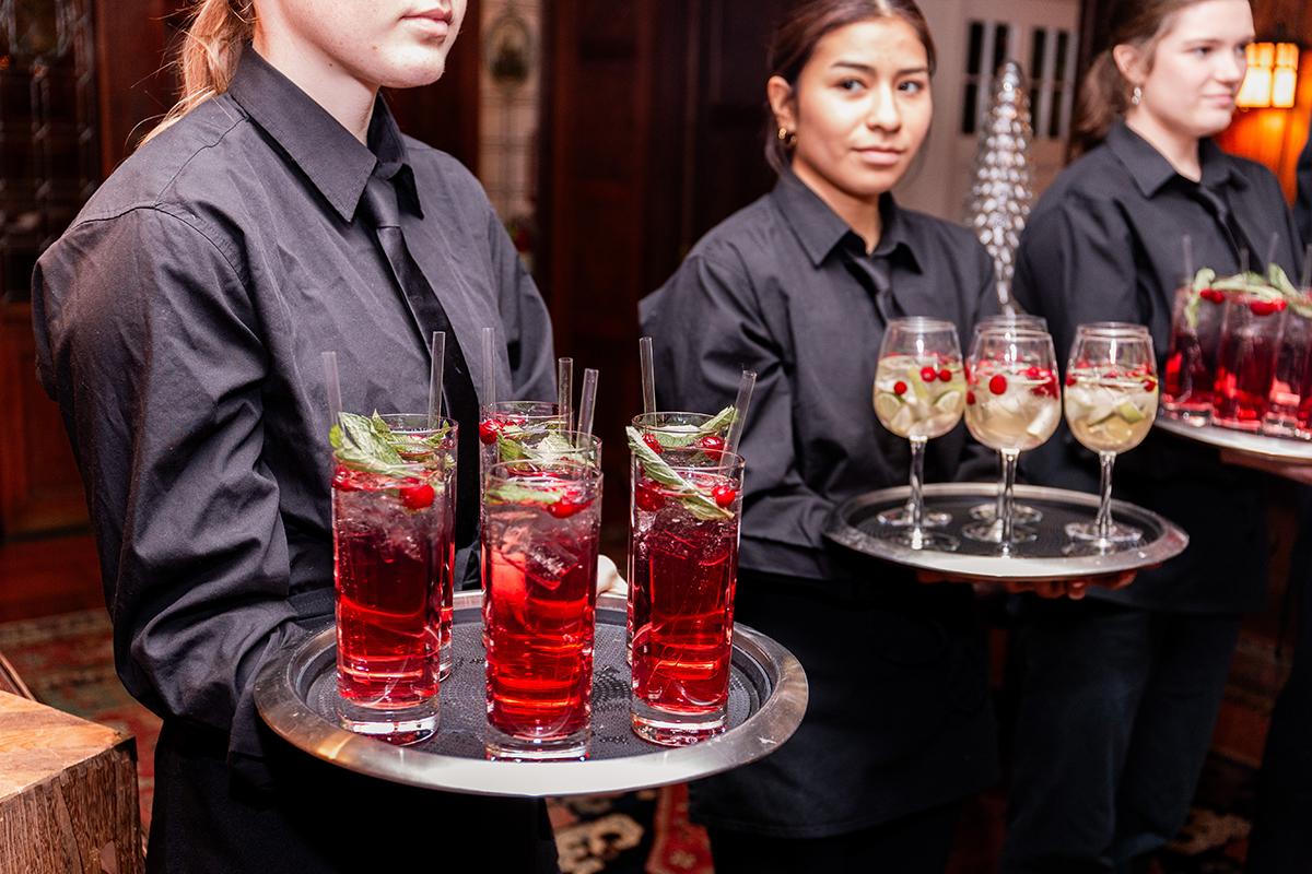 Waitstaff carrying trays of colorful cocktails at an event.