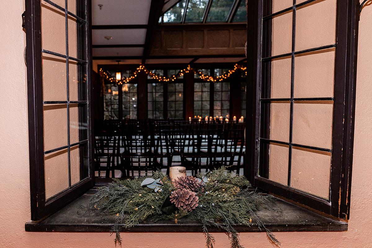 Open window to a room with festive garland lights and empty chairs.