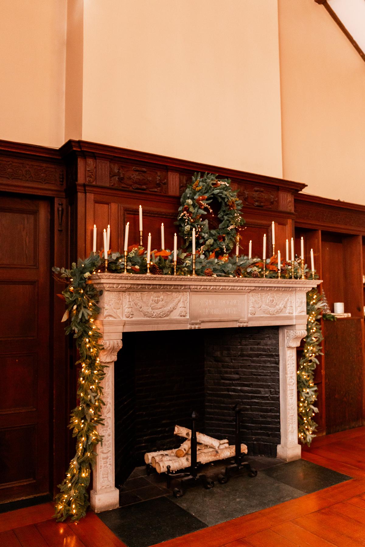Elegant fireplace with wreath, candles, and greenery in a cozy room.
