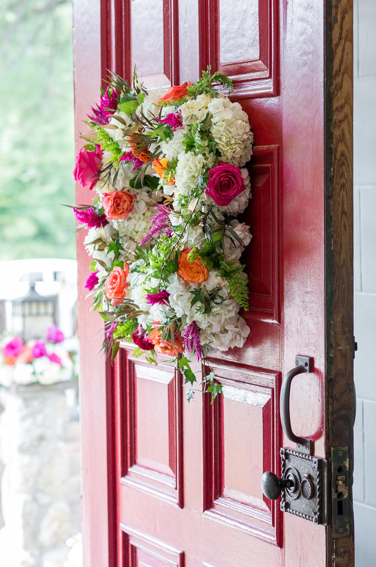 Red door with colorful floral wreath, slightly open.
