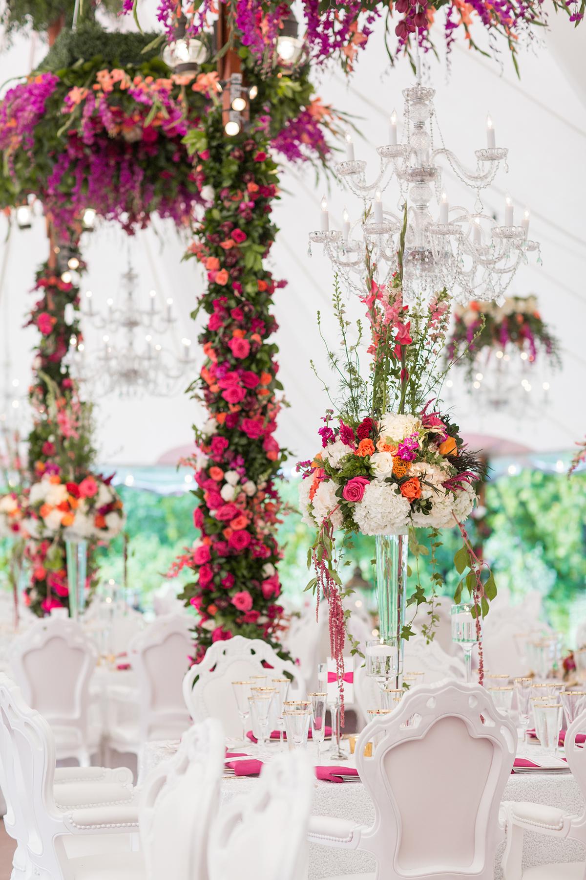 Elegant wedding setup with vibrant florals, chandeliers, and white chairs.