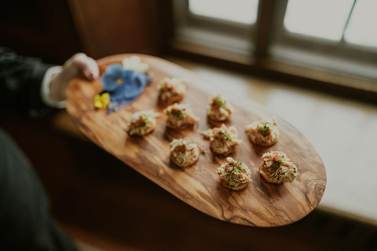 Tray with appetizers and a blue flower garnish near a window.