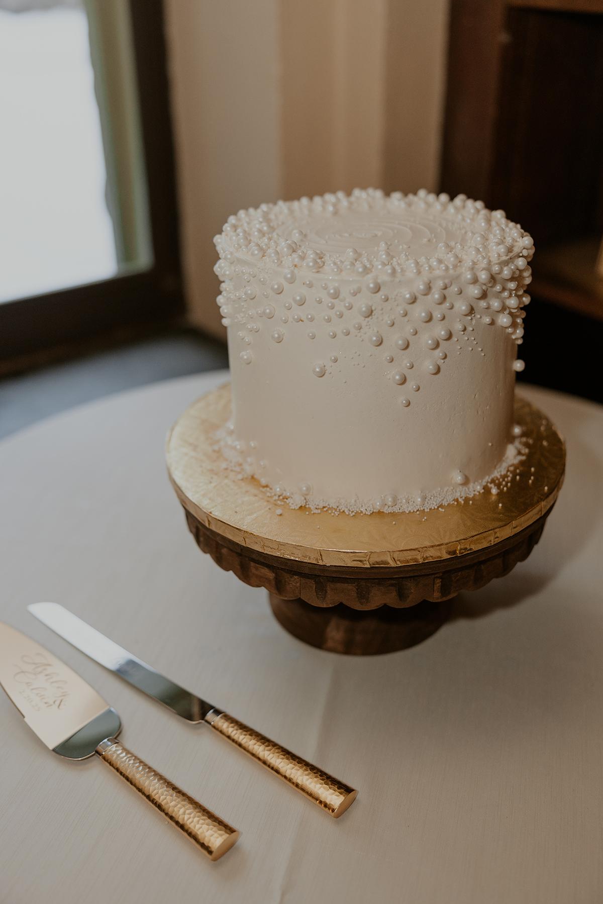 White cake with textured icing on a wooden stand, knife and server beside it.