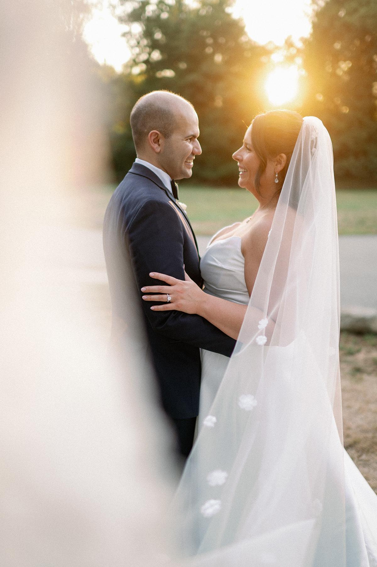 Bride and groom smiling at each other in sunset.