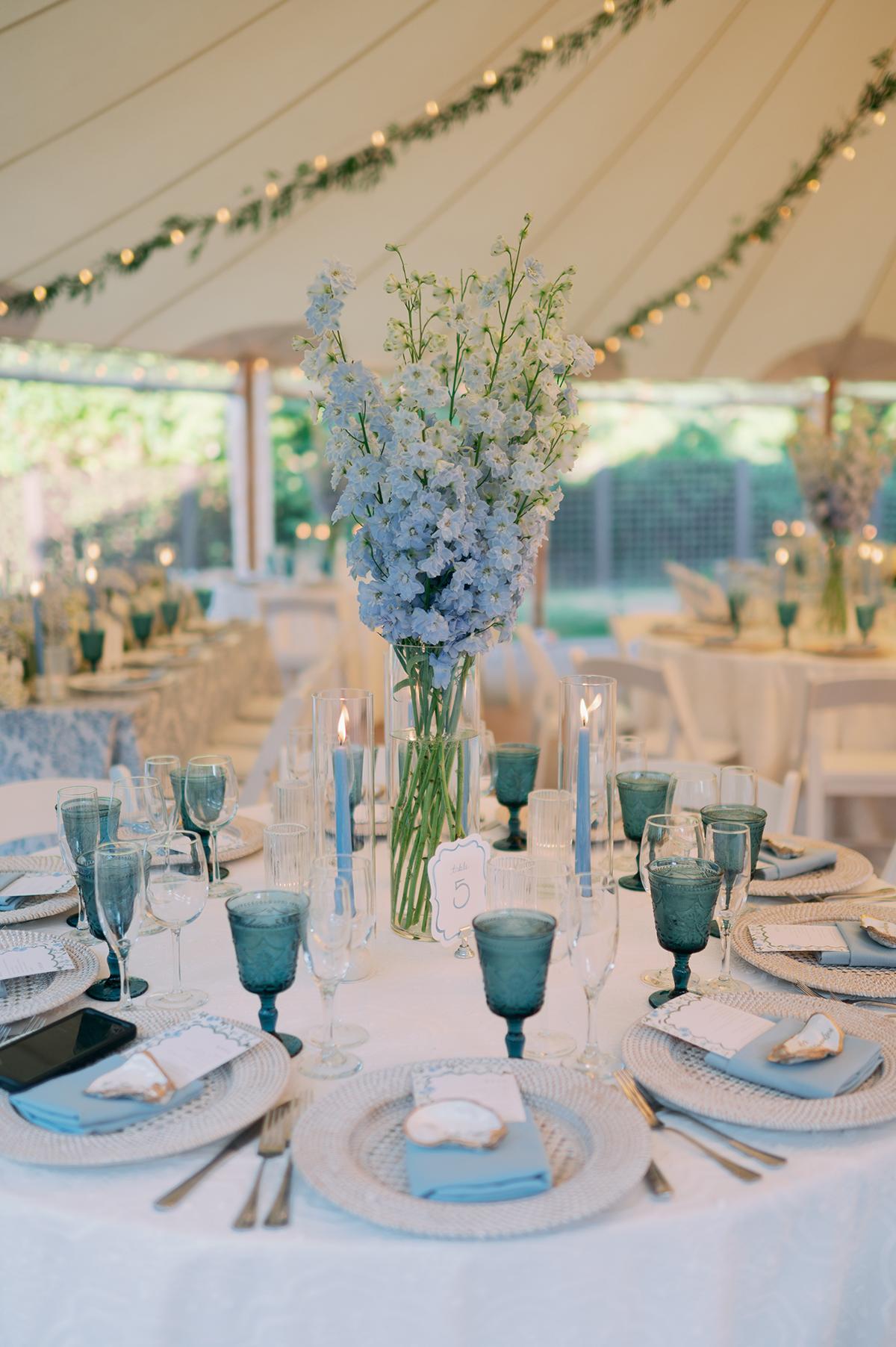 Elegant table setting with blue candles, flowers, and glassware under a tent.
