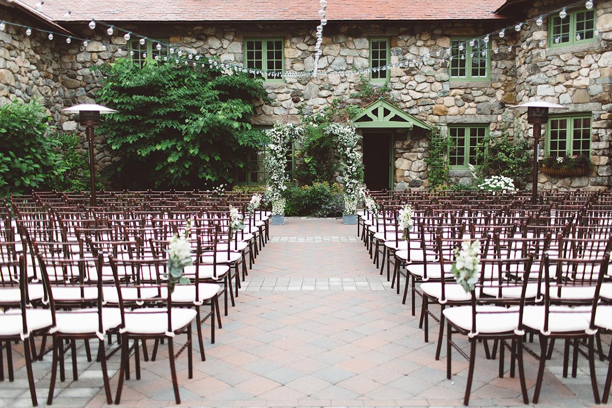 Outdoor wedding setup with rows of chairs facing a stone building.