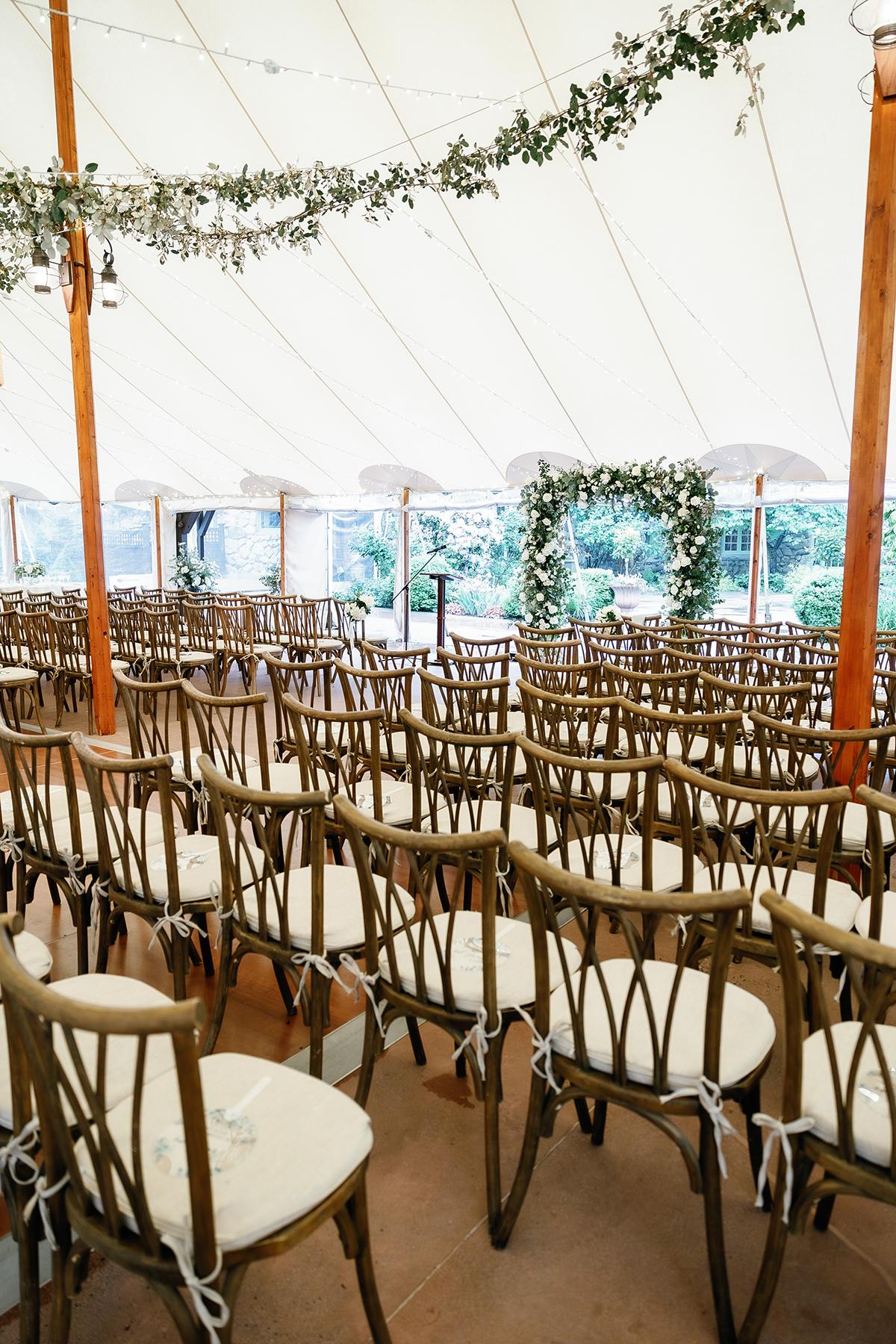 Rows of wooden chairs in a decorated wedding tent.