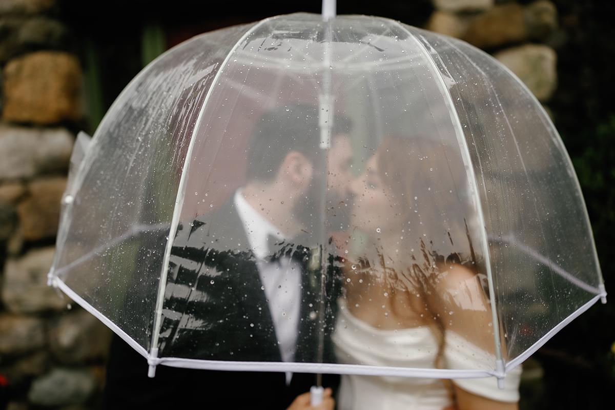 Couple kissing under a clear umbrella on a rainy day.
