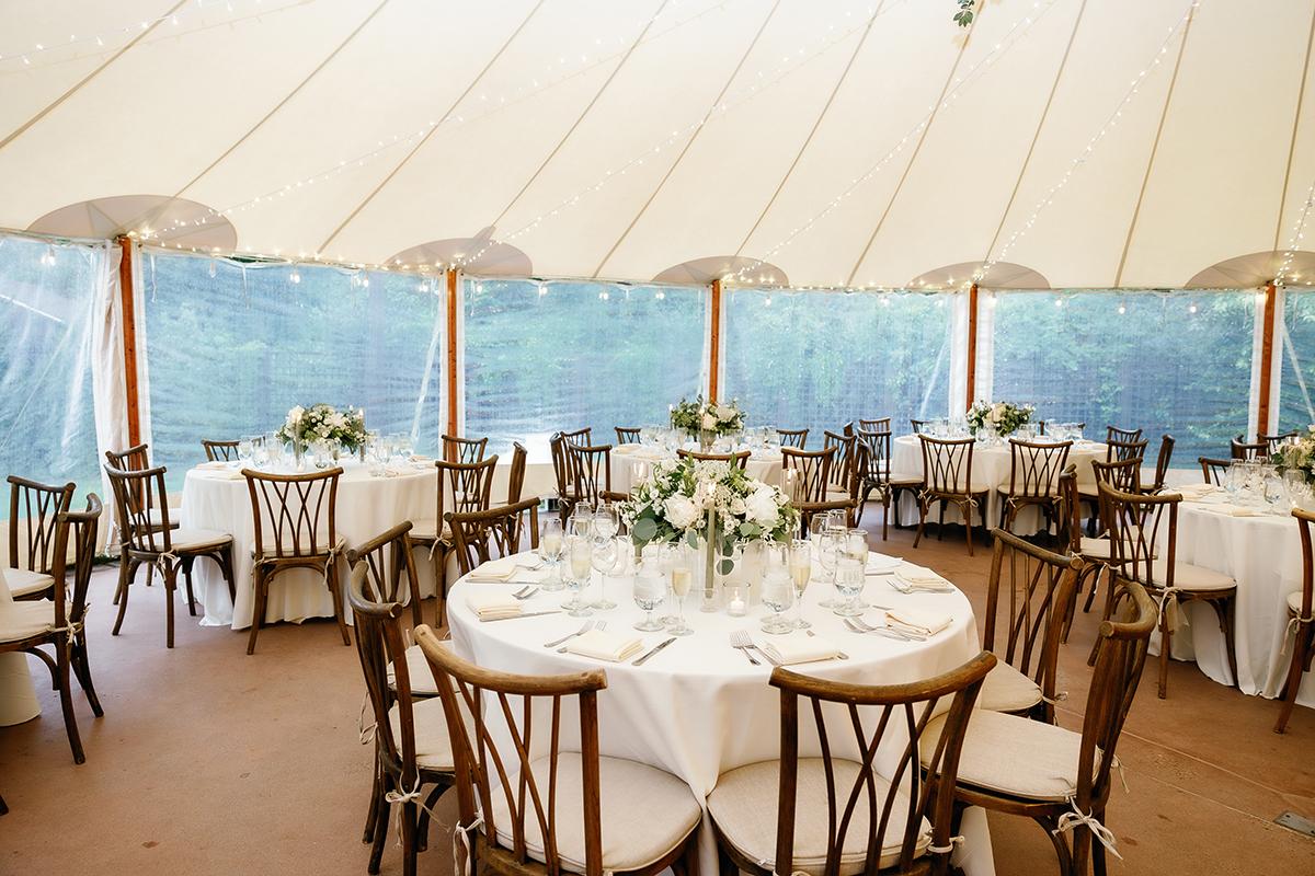 Elegant wedding tent with round tables and floral centerpieces.