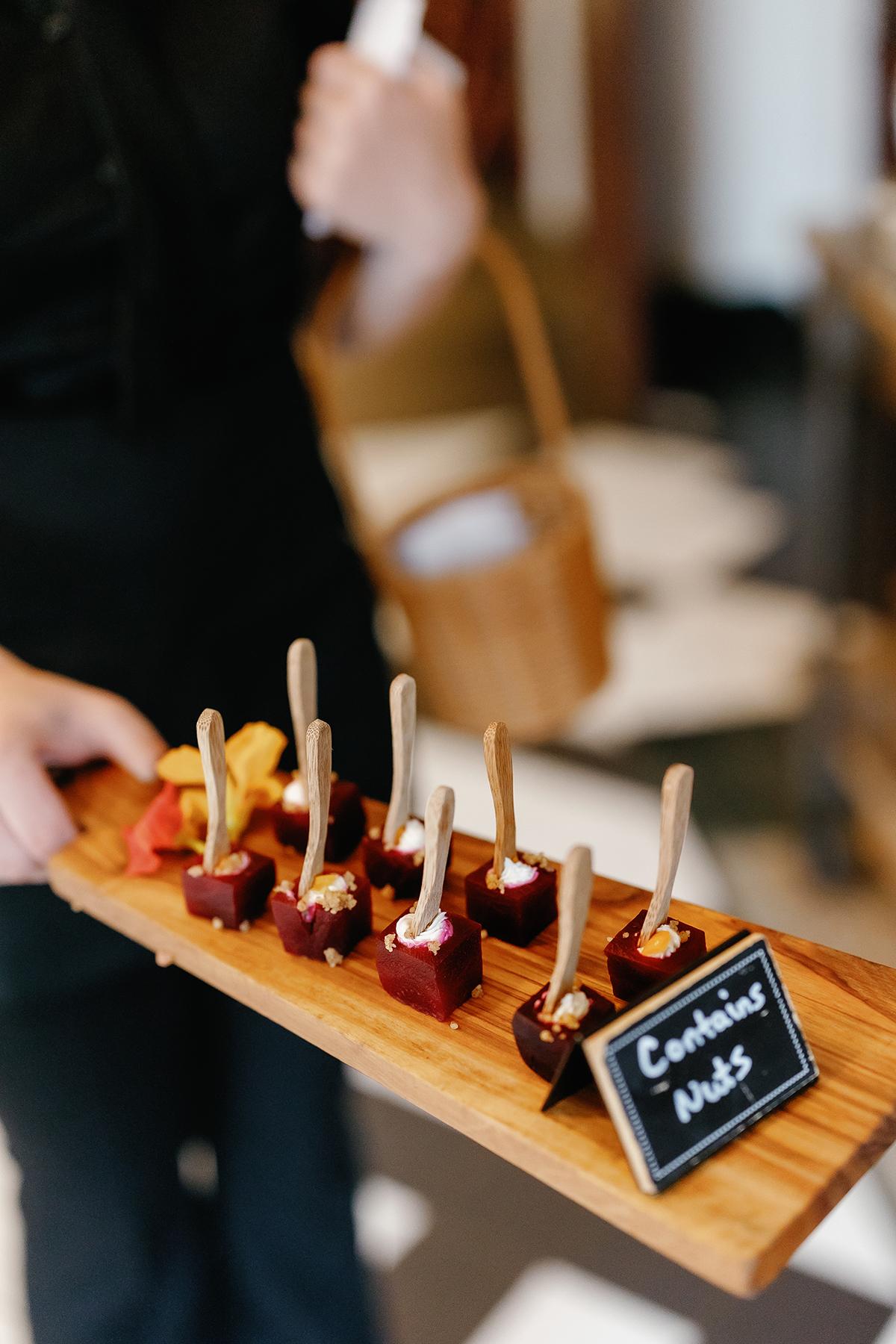 Appetizers served on a wooden tray with small forks and a label.