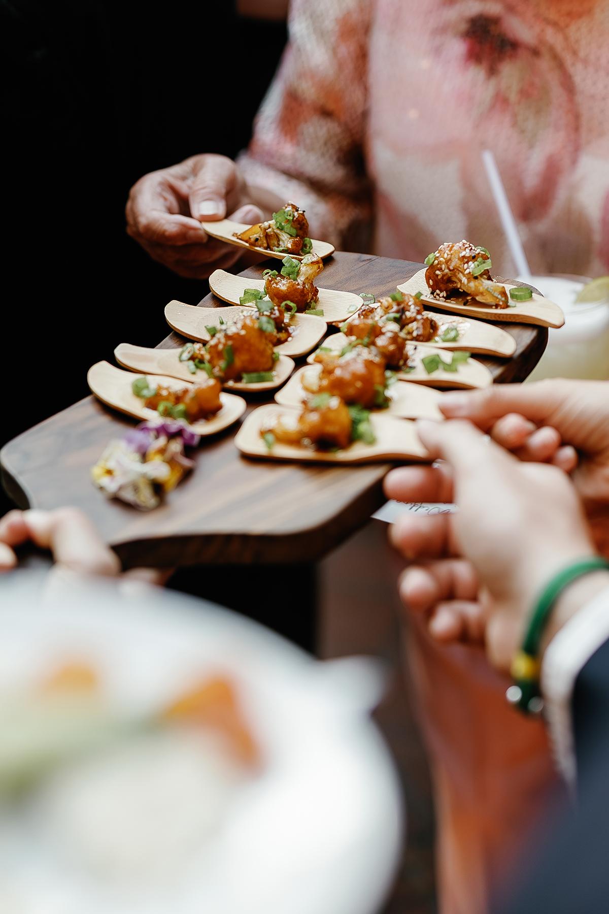 Appetizers on wooden spoons being served on a tray at an event.