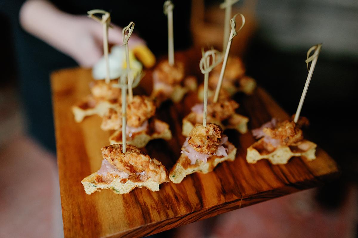 Chicken and waffle appetizers on a wooden tray.