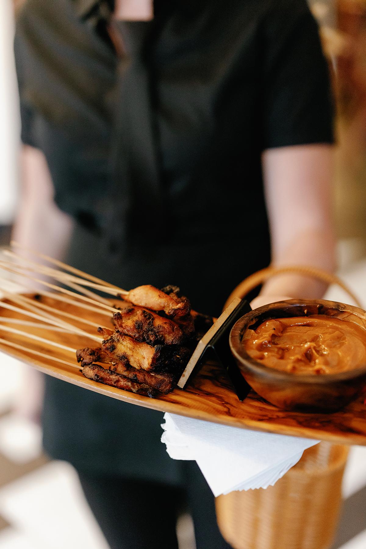 Satay skewers with sauce served on a wooden platter.