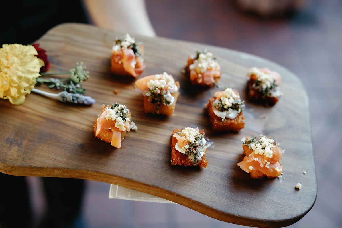 Appetizers on a wooden board with herbs and a yellow flower.
