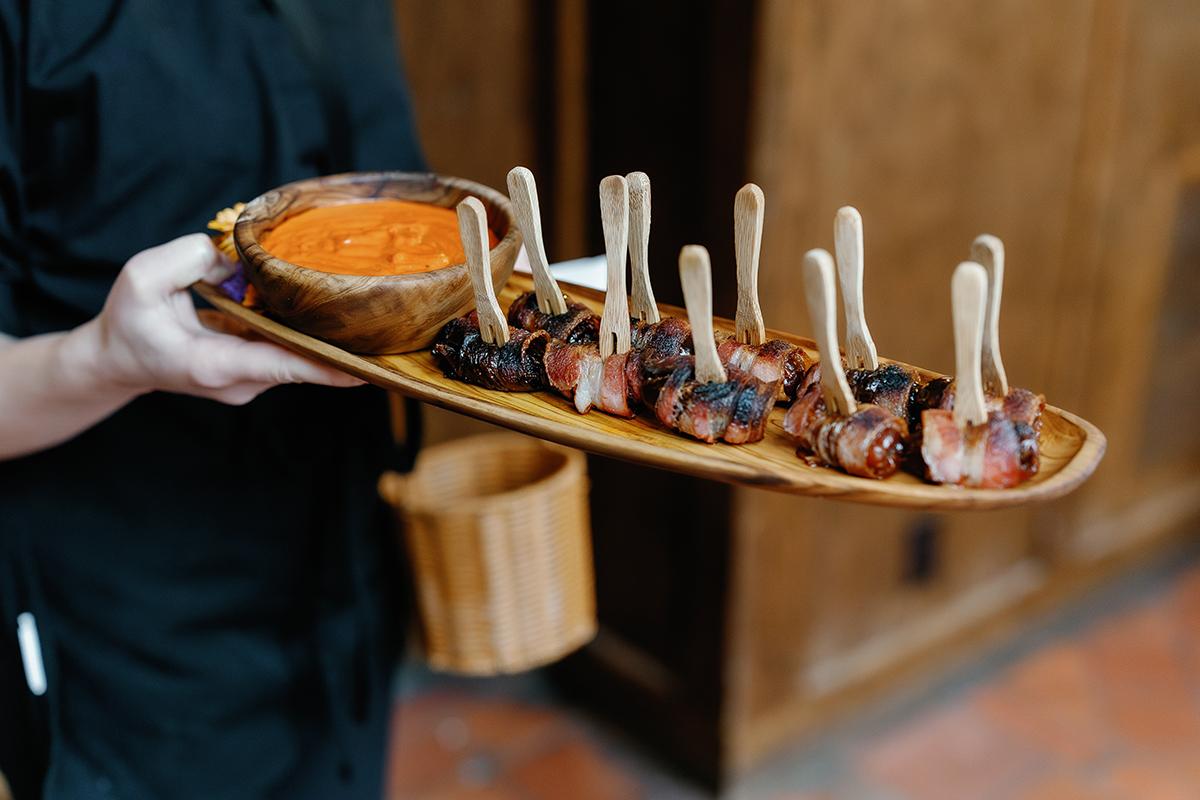 Server holding a tray of appetizers with a dipping sauce.