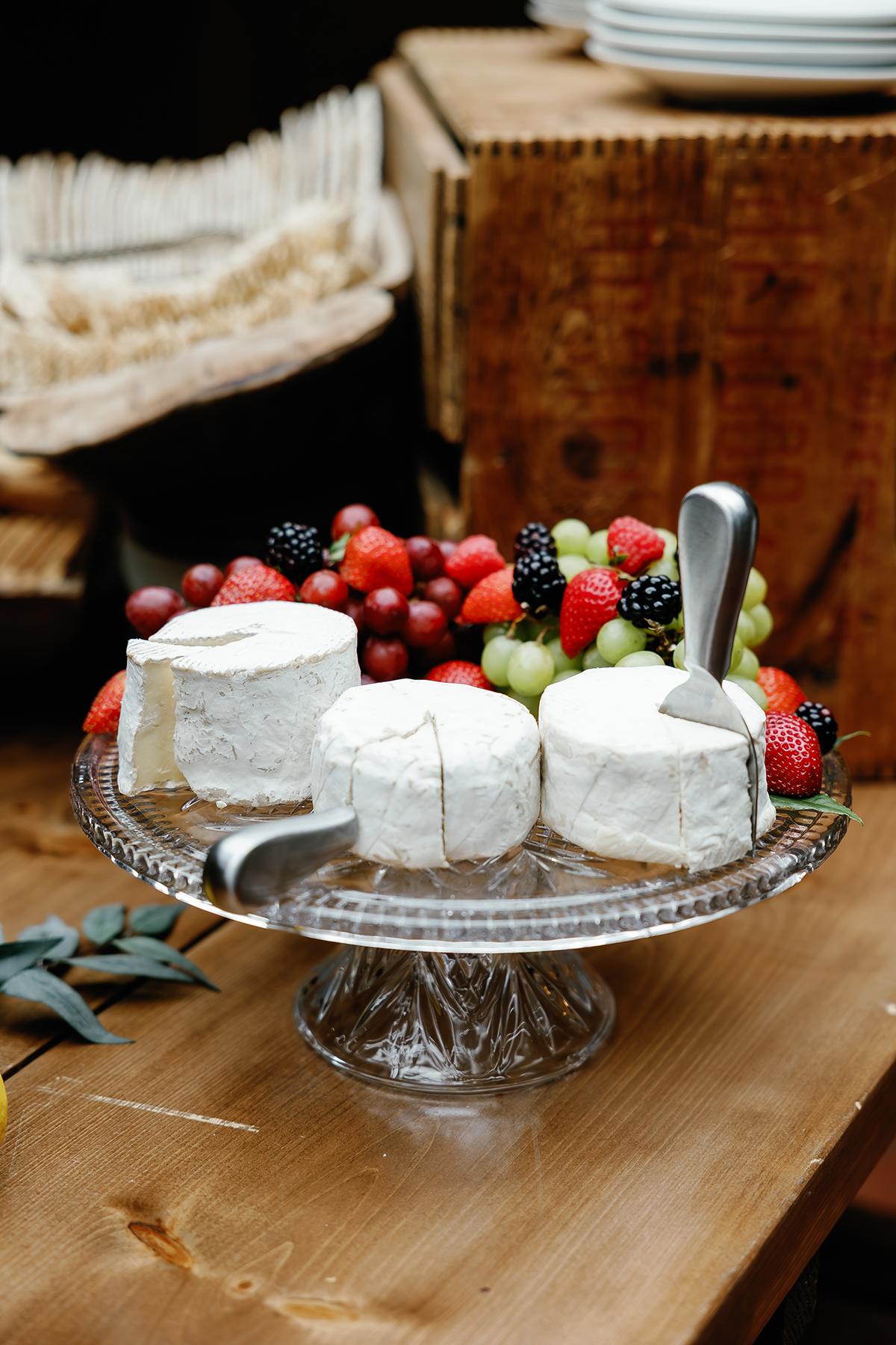 Cheese wheels on a glass platter with assorted berries.