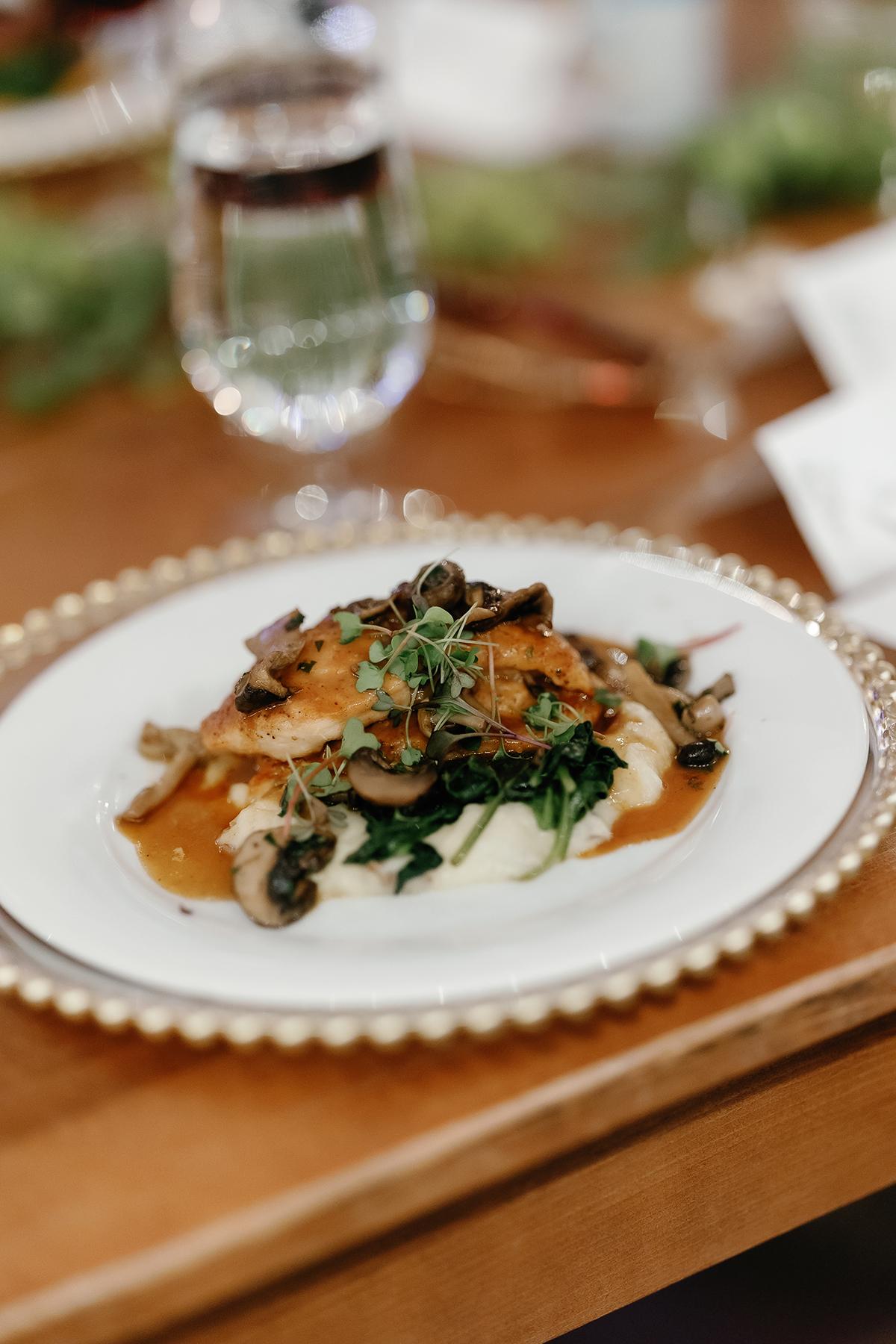 Plate of grilled chicken with mushrooms and greens, garnished with herbs.