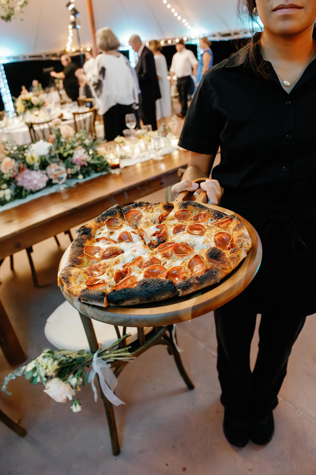 Server holding a pepperoni pizza at an elegant event.