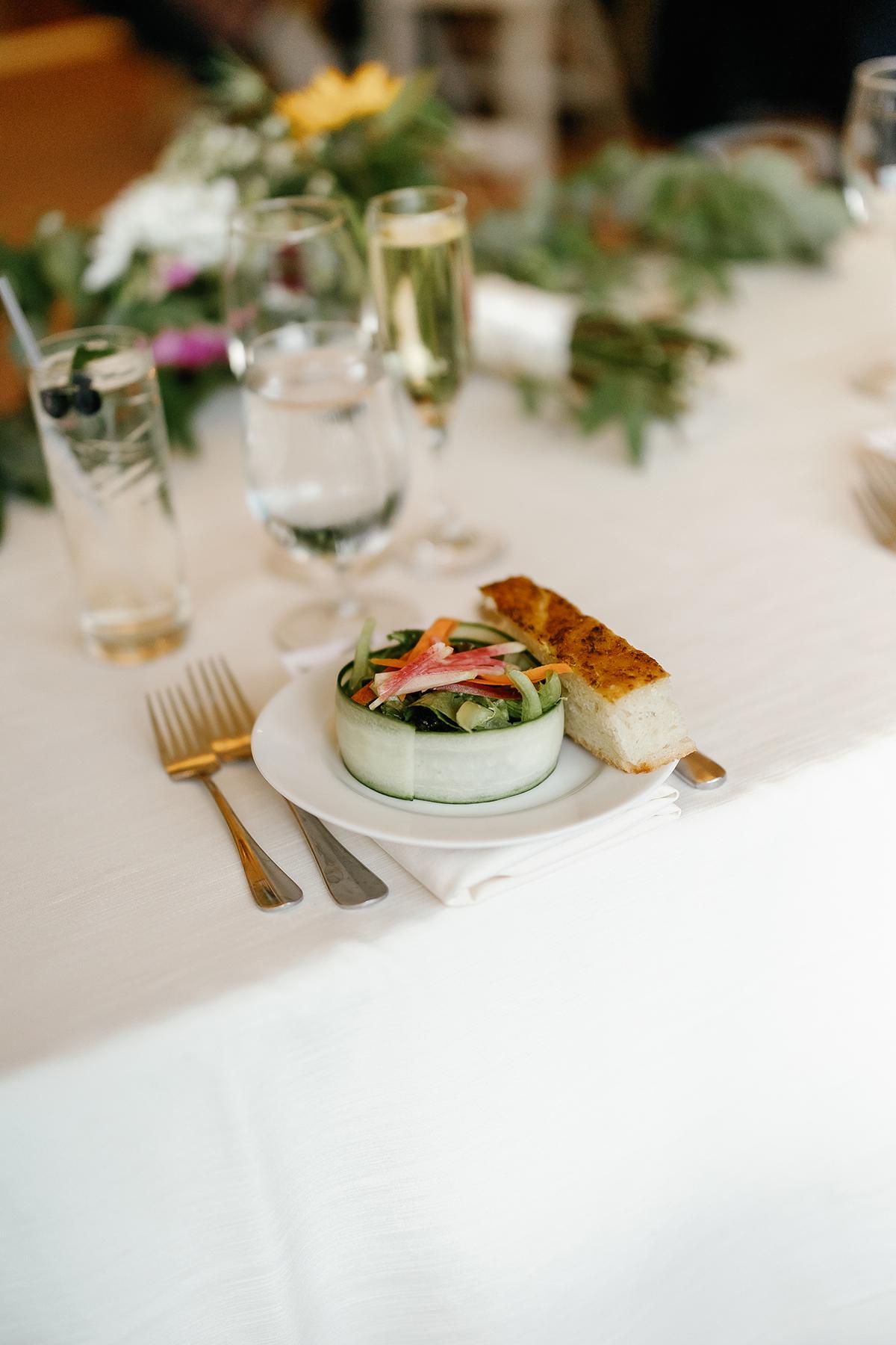 Plate with salad, bread, and a fork on a white tablecloth.