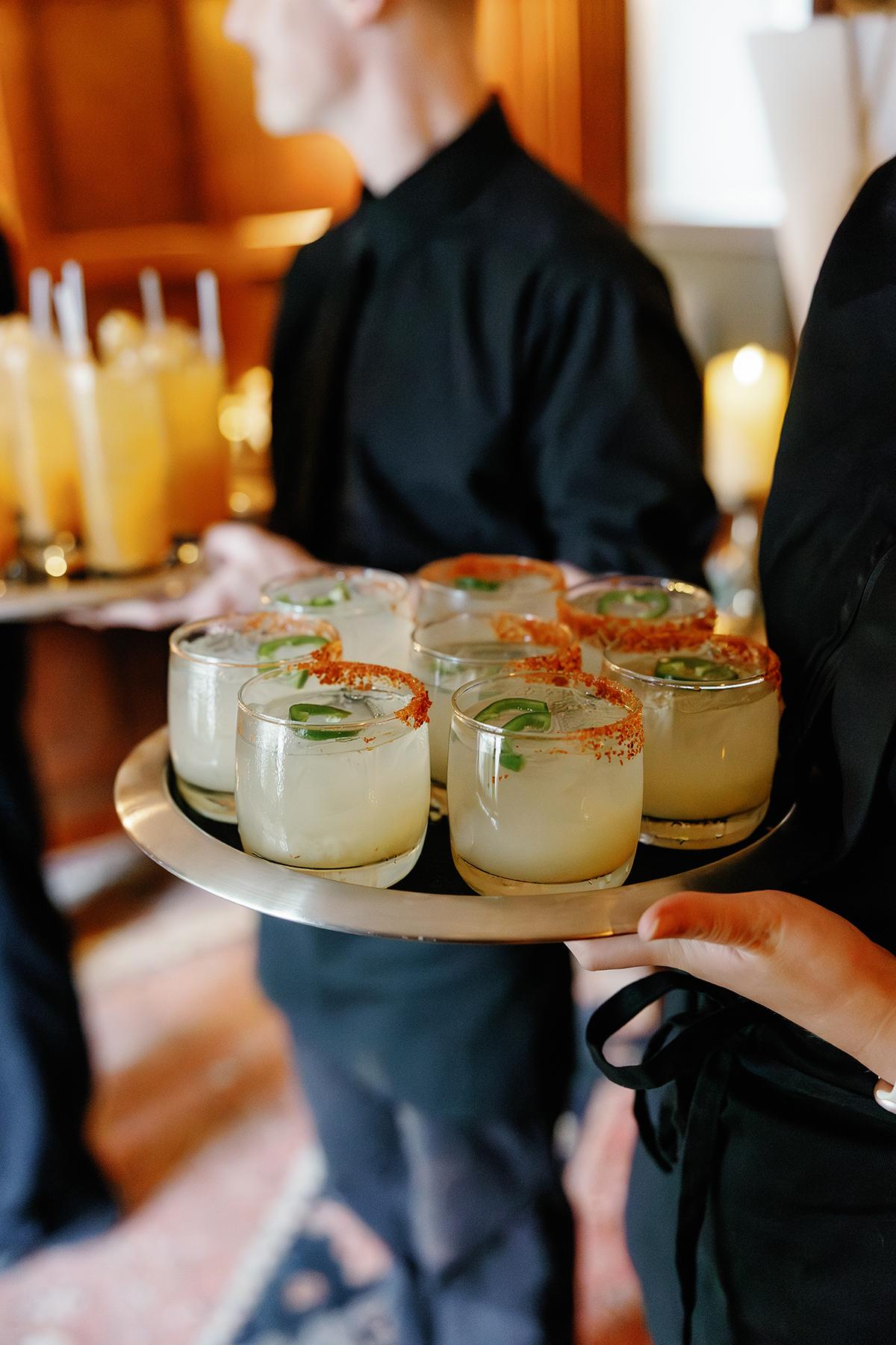 Tray of lemon cocktails with mint leaves, held by servers in black attire.