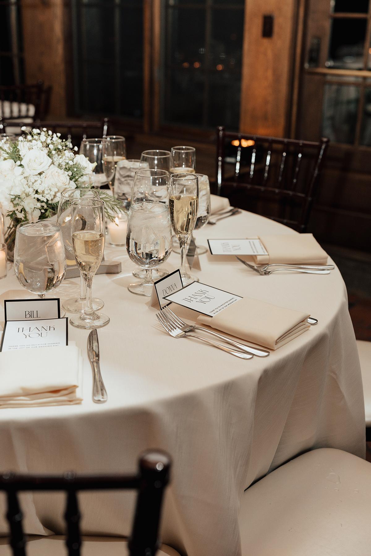 Round table with white tablecloth, elegant glassware, and floral centerpiece.