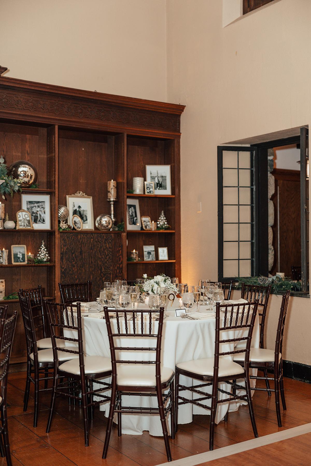 Elegant dining table with wooden chairs set for an event, in a warmly lit room.