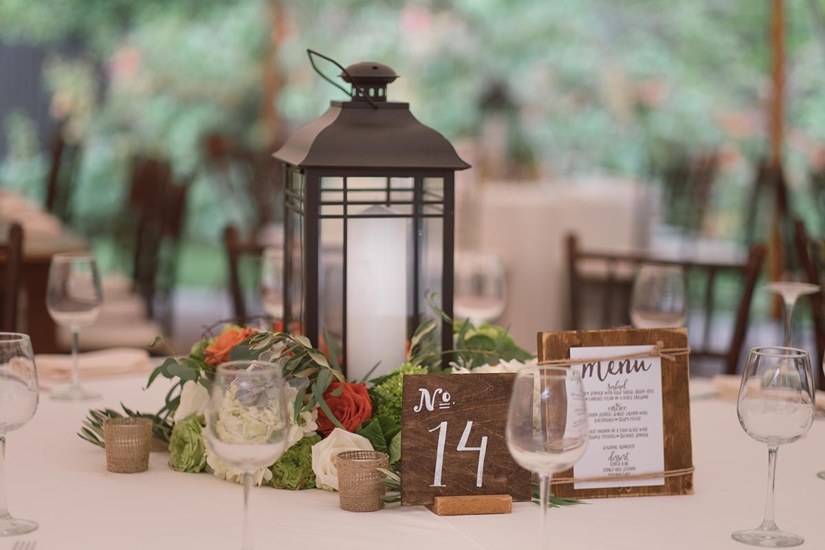 Centerpiece with lantern, greenery, and table number 14 on a set dining table.