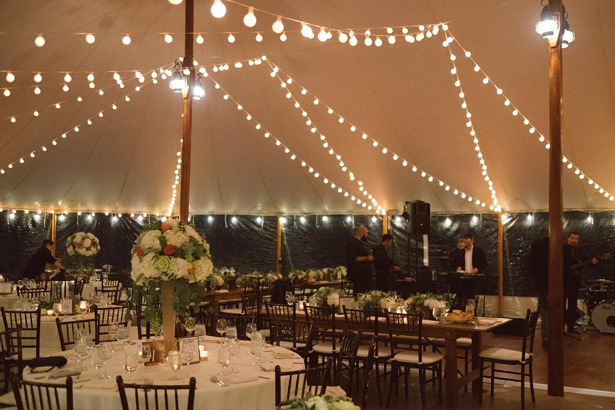 Elegant tent wedding reception with string lights and flower centerpieces.