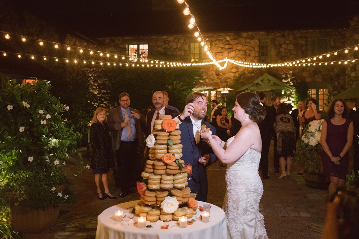 Bride and groom feed each other donuts at an outdoor night wedding reception.