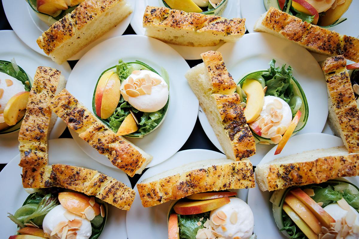Plates with salads, burrata cheese, peach slices, and bread wedges arranged neatly.
