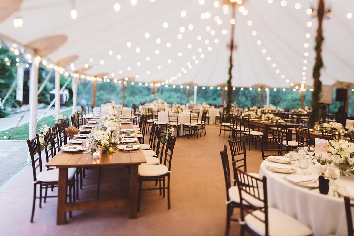 Outdoor wedding reception under a canopy, tables elegantly set, string lights overhead.