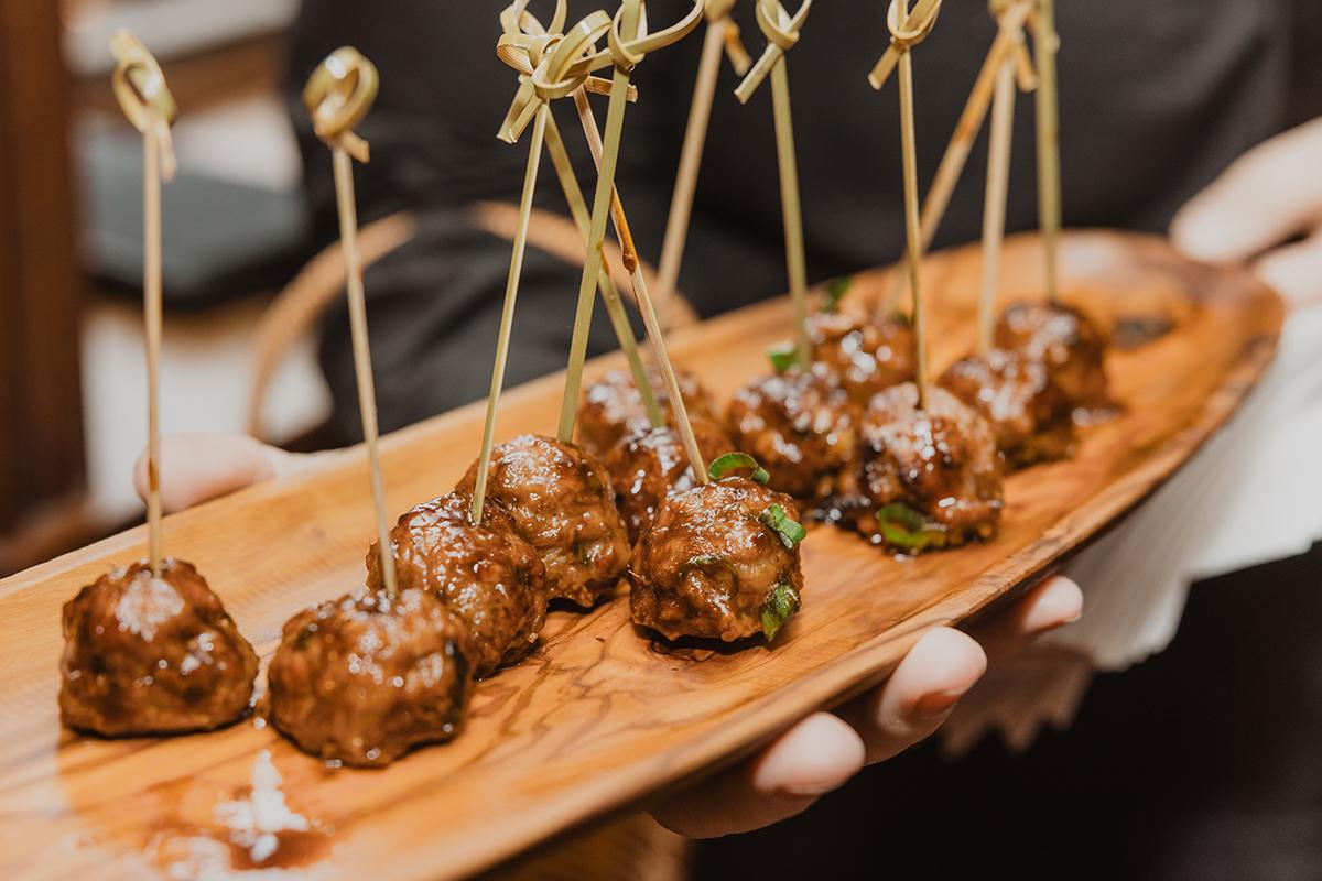 Skewered meatballs on a wooden serving platter.