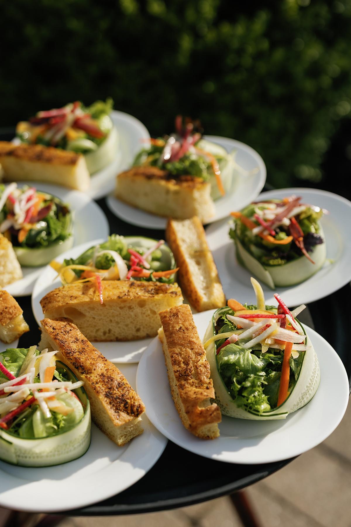 Plates of fresh salads and breadsticks on a table outdoors.
